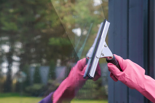 gloved hand holding a window squeegee to clean a window