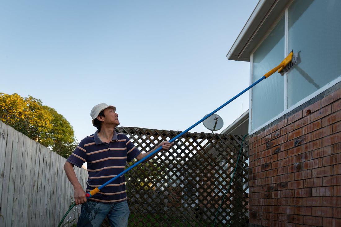 Man washing windows with a long pole and brush