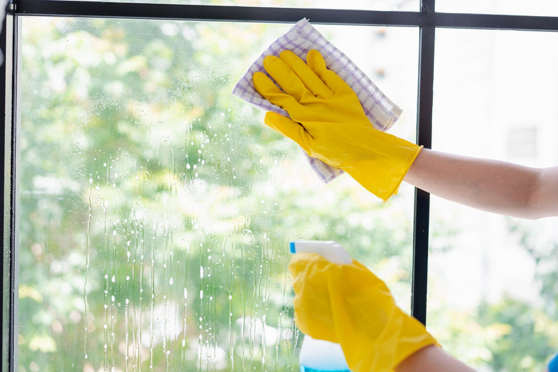Close up of yellow gloved hands using a spray bottle and cloth to clean a window