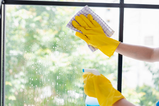 Close up of yellow gloved hands using a spray bottle and cloth to clean a window