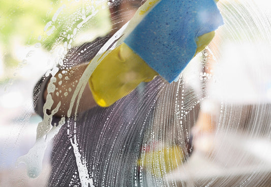 window cleaner wearing yellow gloves using a soapy blue sponge