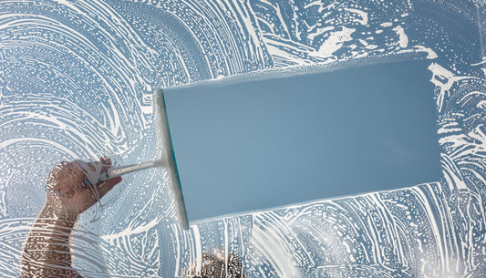 a hand holding a window squeegee handle clearing a soapy window