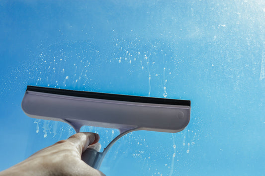 Hand using window squeegee on glass against blue sky
